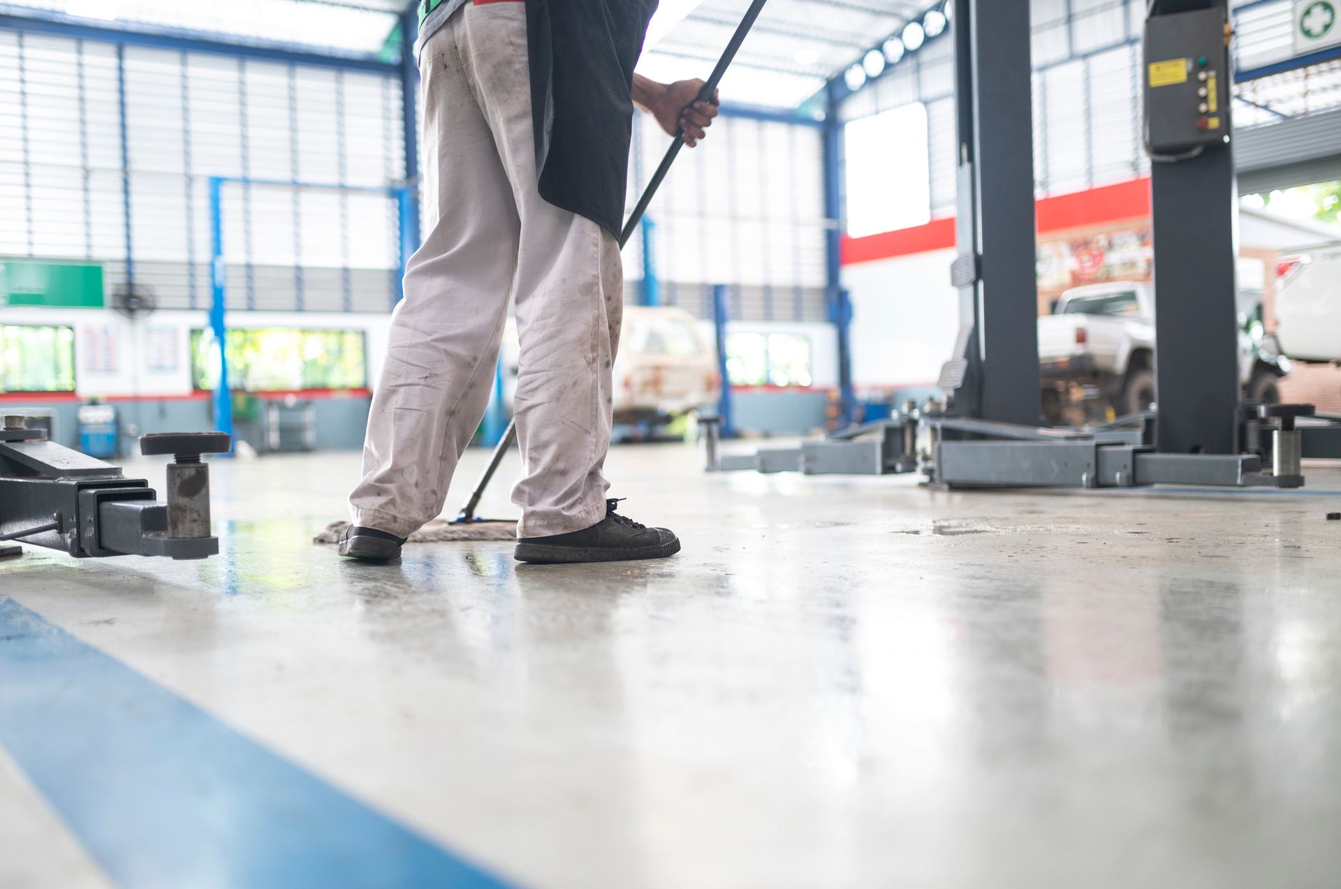 Mechanic mopping a garage floor, wearing work pants and holding a mop handle.
