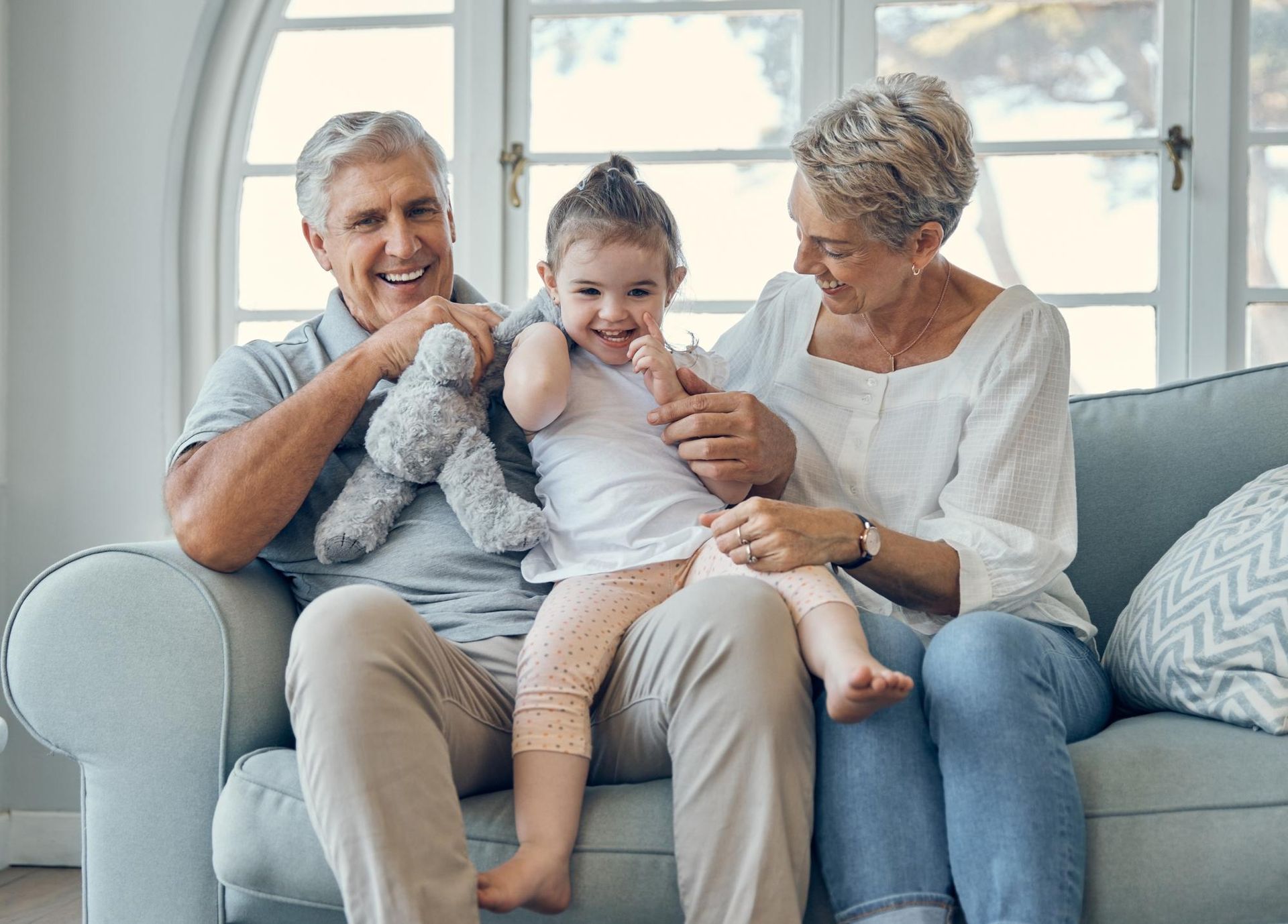 Grandparents sitting on a couch with a smiling toddler; the little girl is on their laps.
