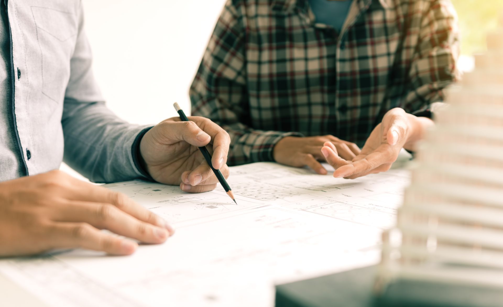 Two people reviewing blueprints, discussing plans at a desk. One points a pencil.