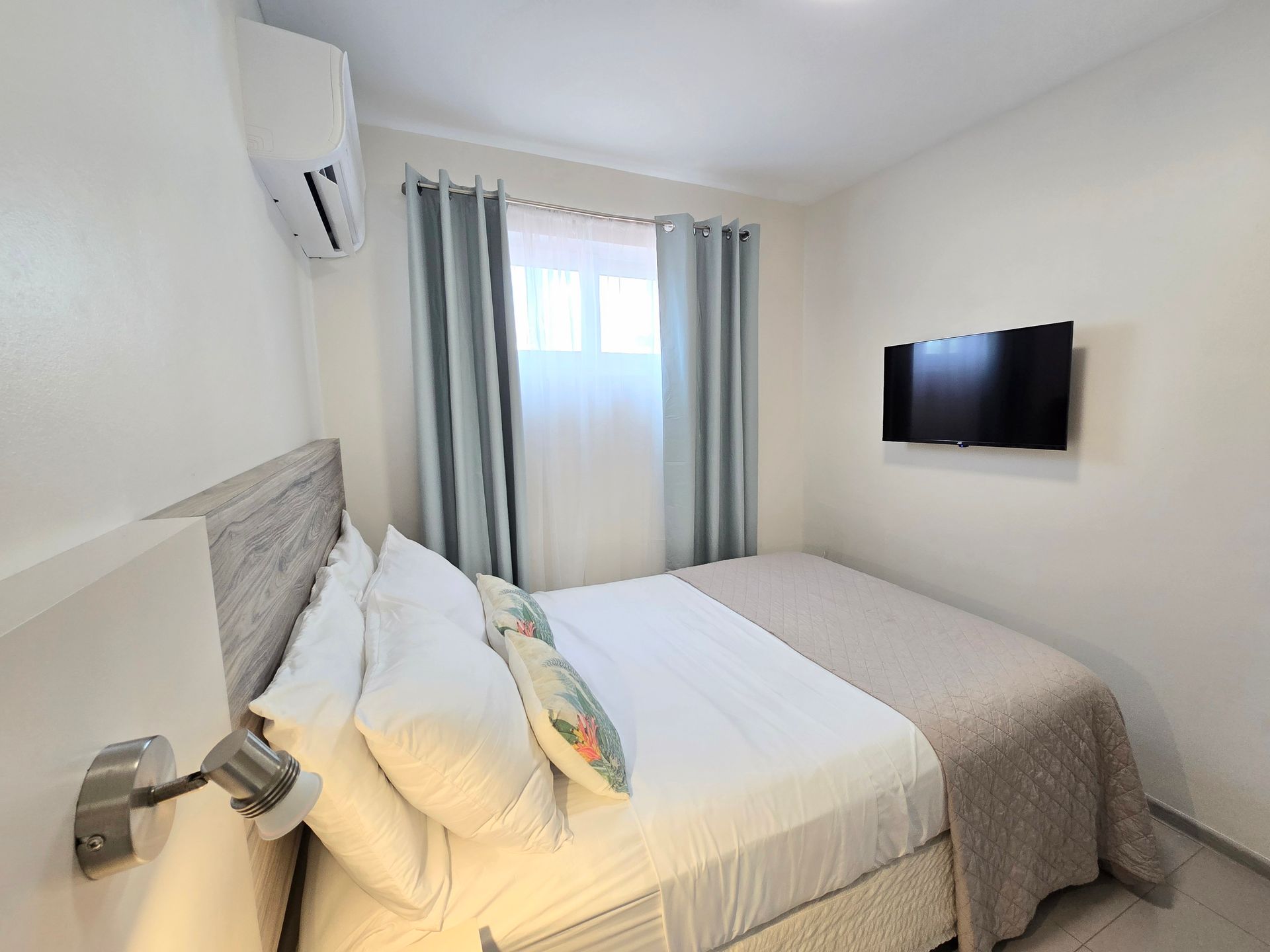 A bedroom with a bed , nightstand , mirror and window.