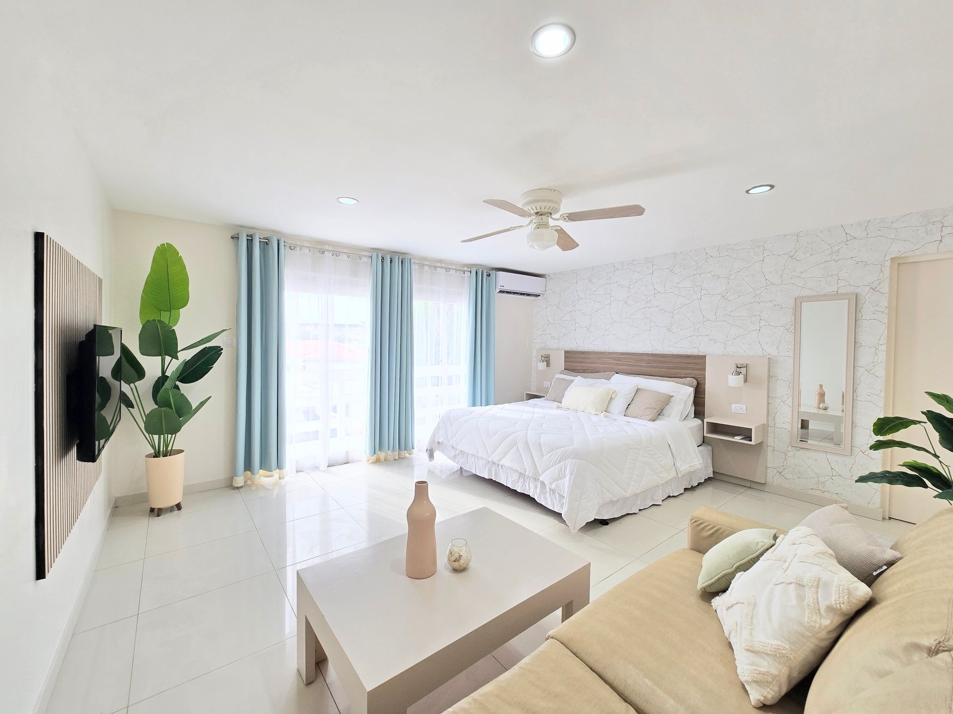 A bedroom with a bed , couch , television and ceiling fan.