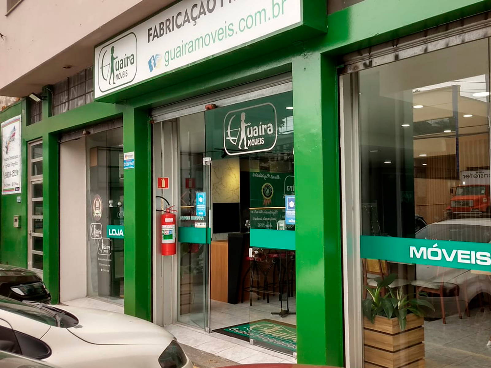 Um carro branco está estacionado em frente a um prédio verde.