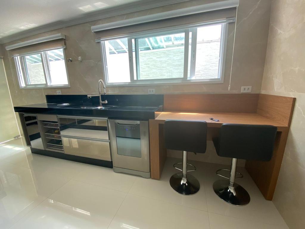 Uma cozinha com bancos, pia, geladeira e mesa.