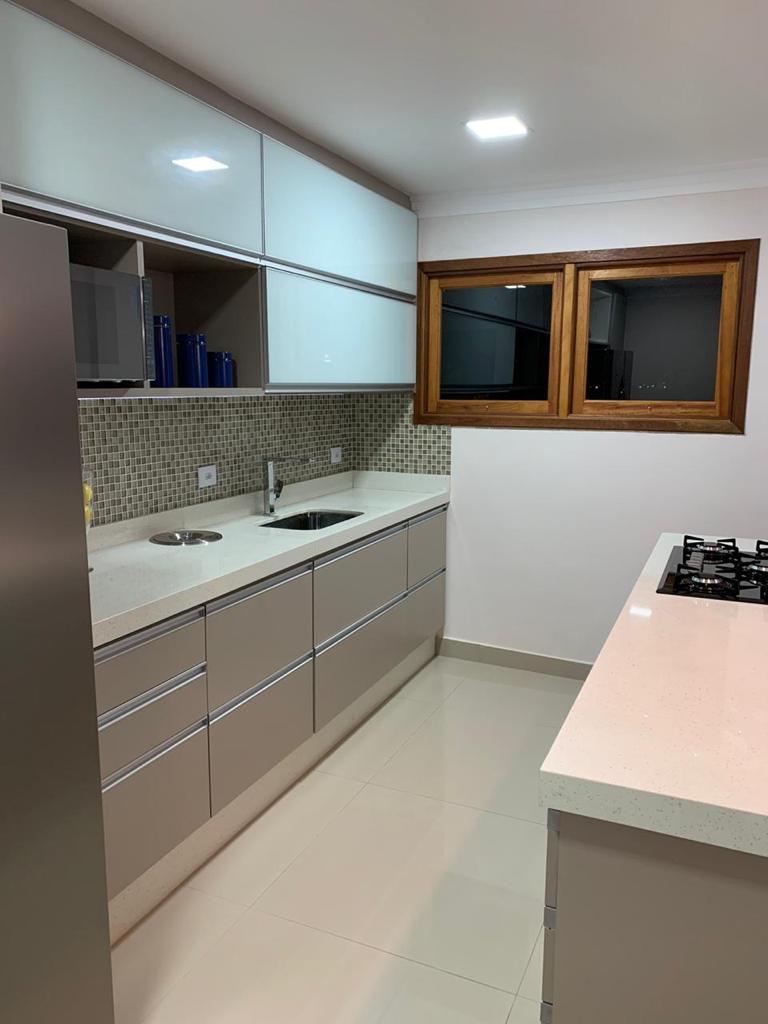 Uma cozinha com eletrodomésticos de aço inoxidável, bancadas brancas, pia e janela.