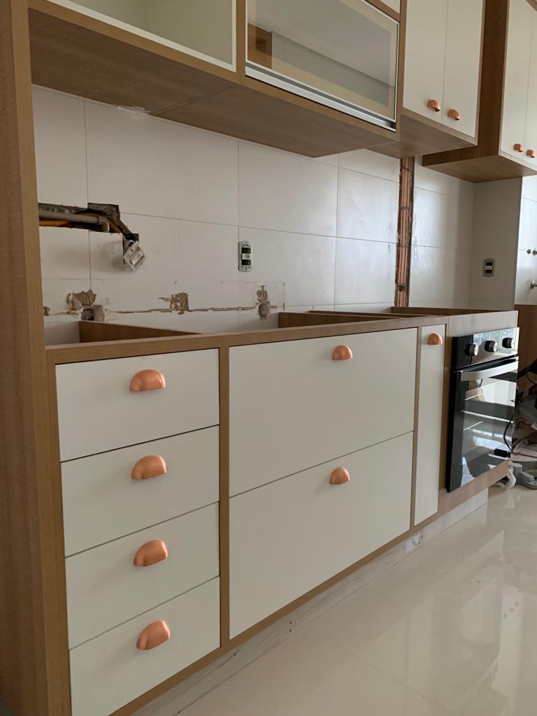 Uma cozinha com armários brancos e puxadores de cobre.