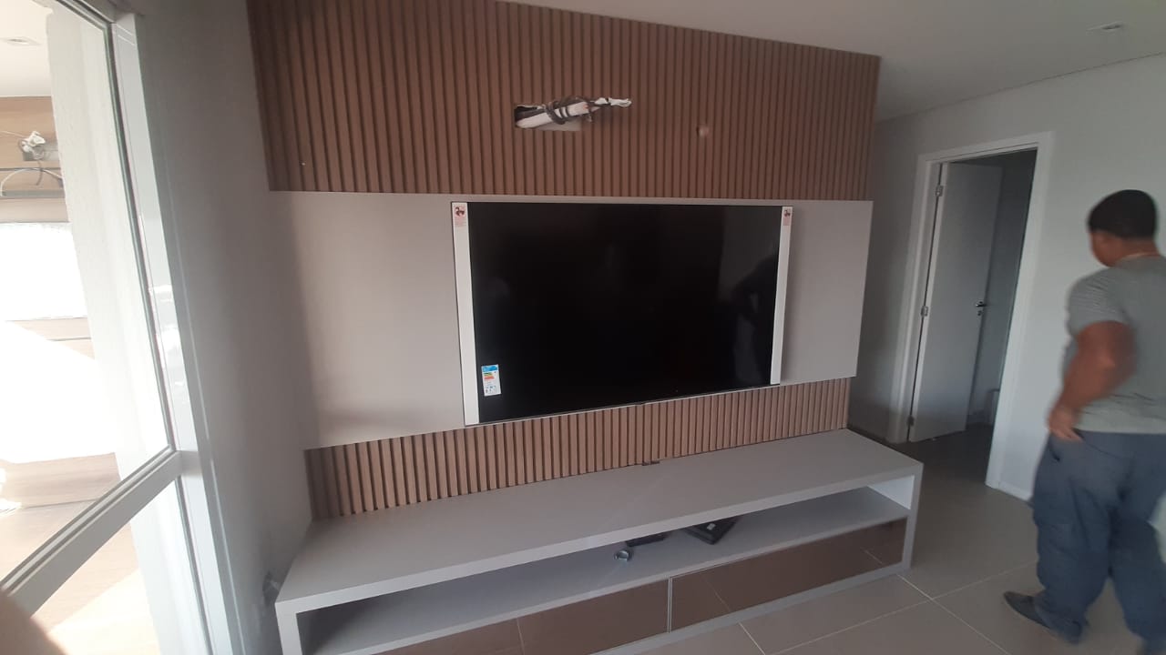 Um homem está parado em frente a uma televisão montada na parede.