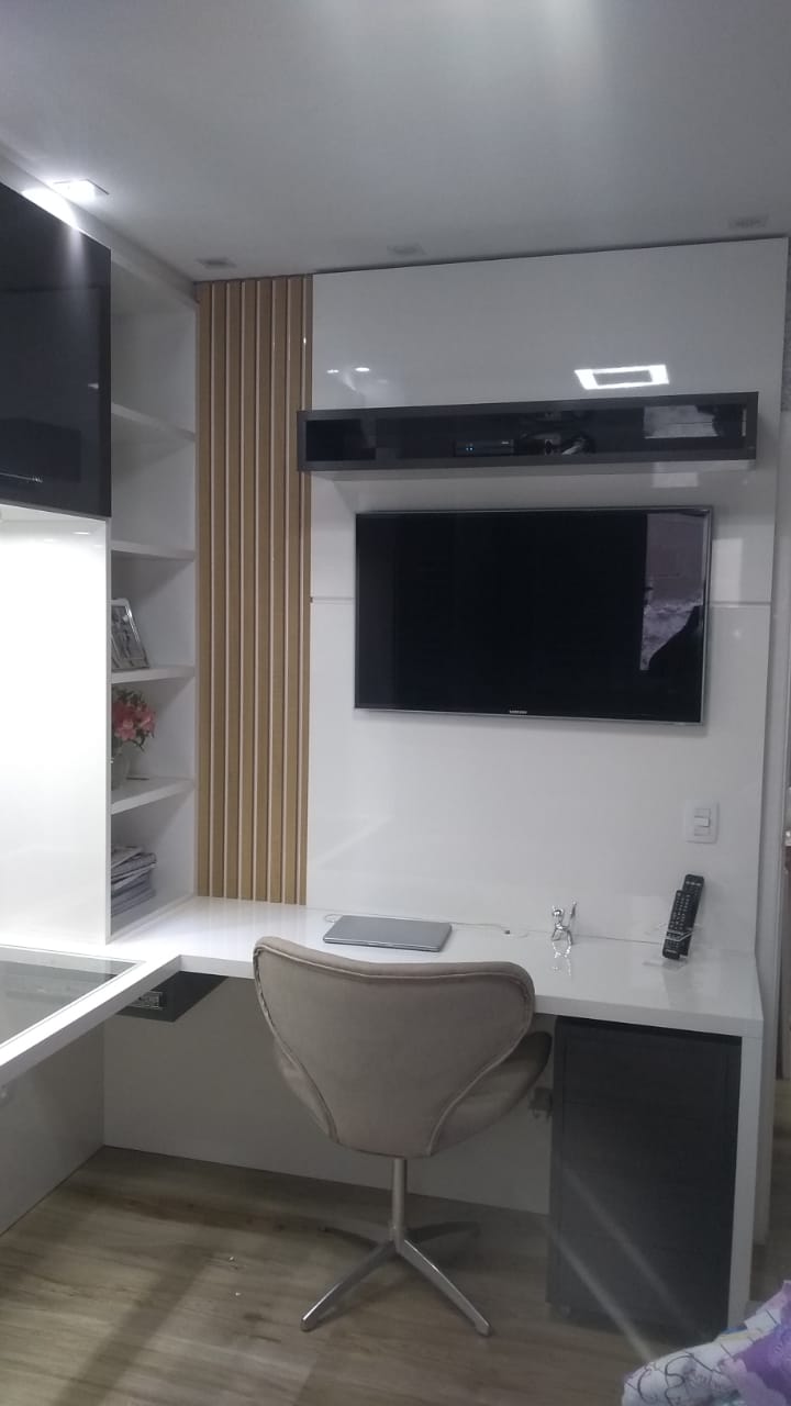 Há uma mesa com uma cadeira e uma televisão na parede.