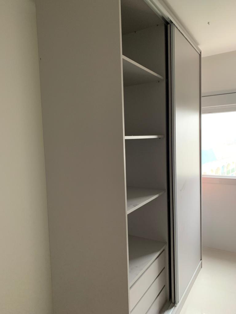 Um guarda-roupa branco com portas de correr e prateleiras num quarto.