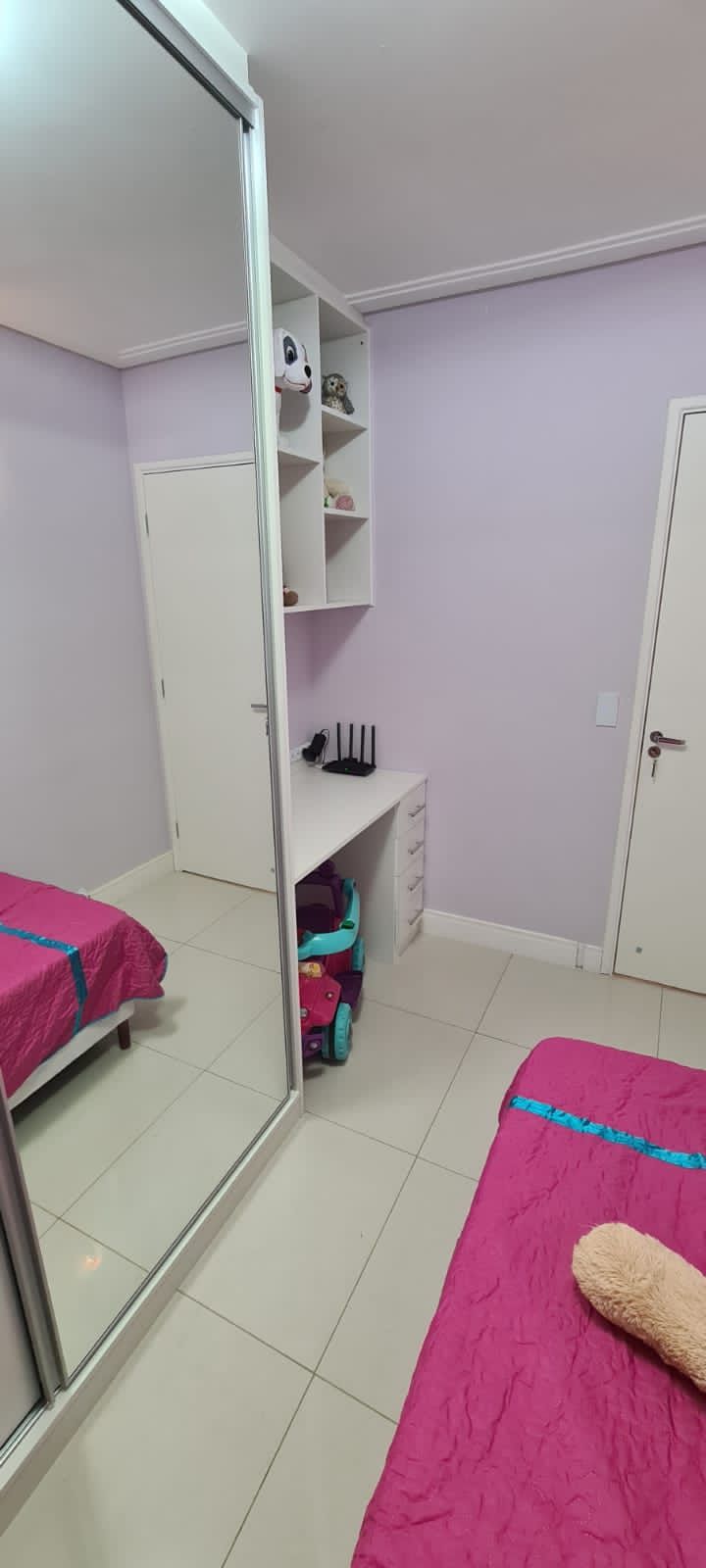 Um quarto com cama, escrivaninha, espelho e paredes roxas.