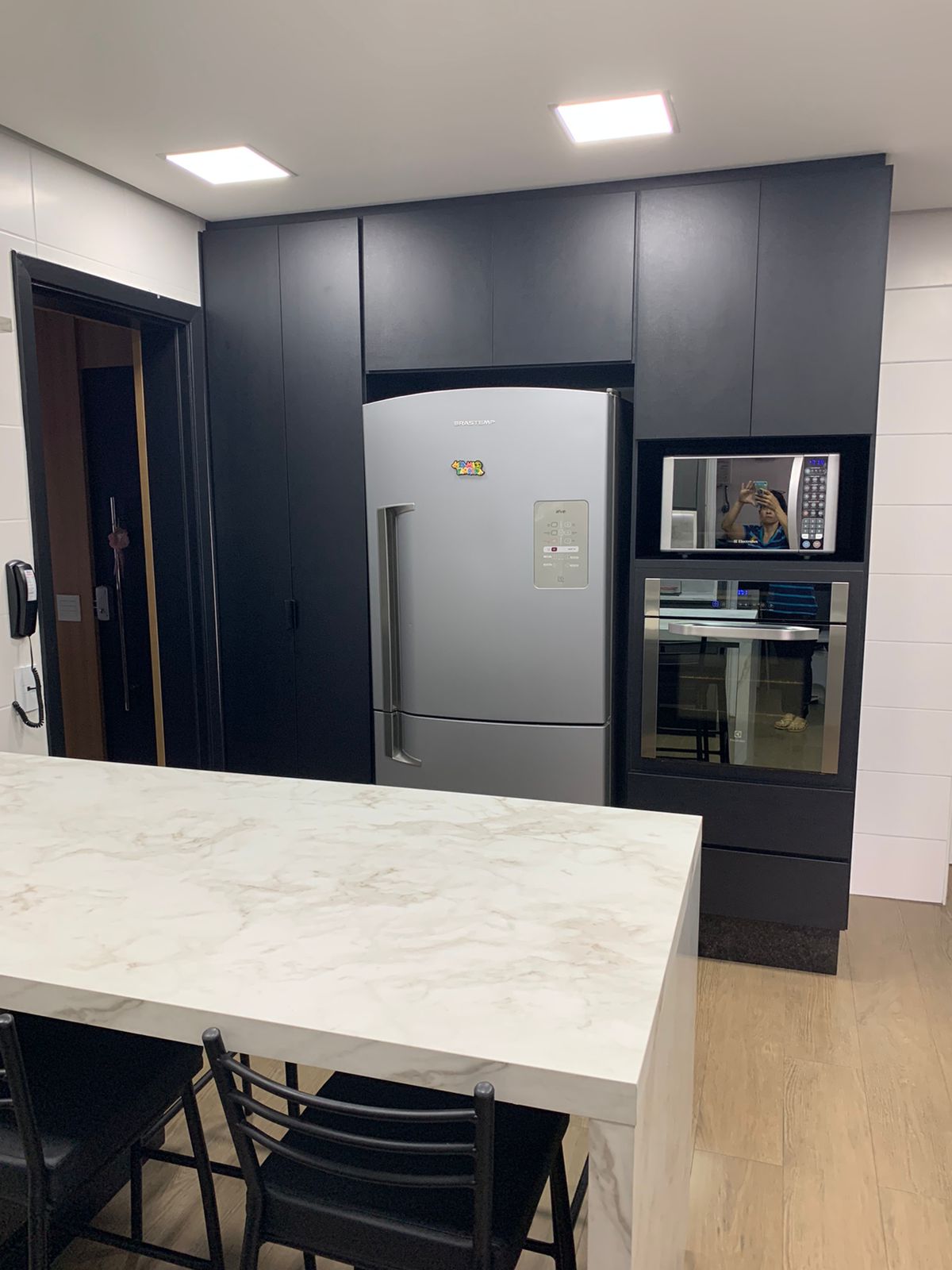 Uma cozinha com armários pretos, geladeira, micro-ondas e mesa.