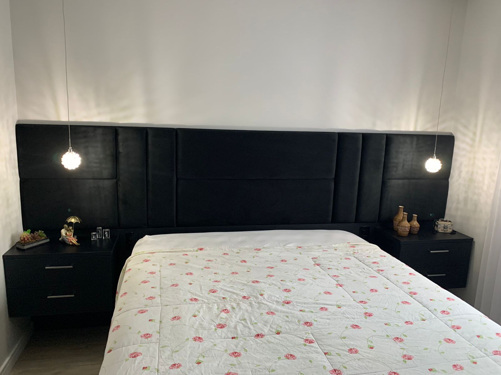 Um quarto com cama, mesinhas de cabeceira e cabeceira preta.