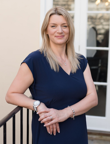 Kelly stands facing the camera and smiling