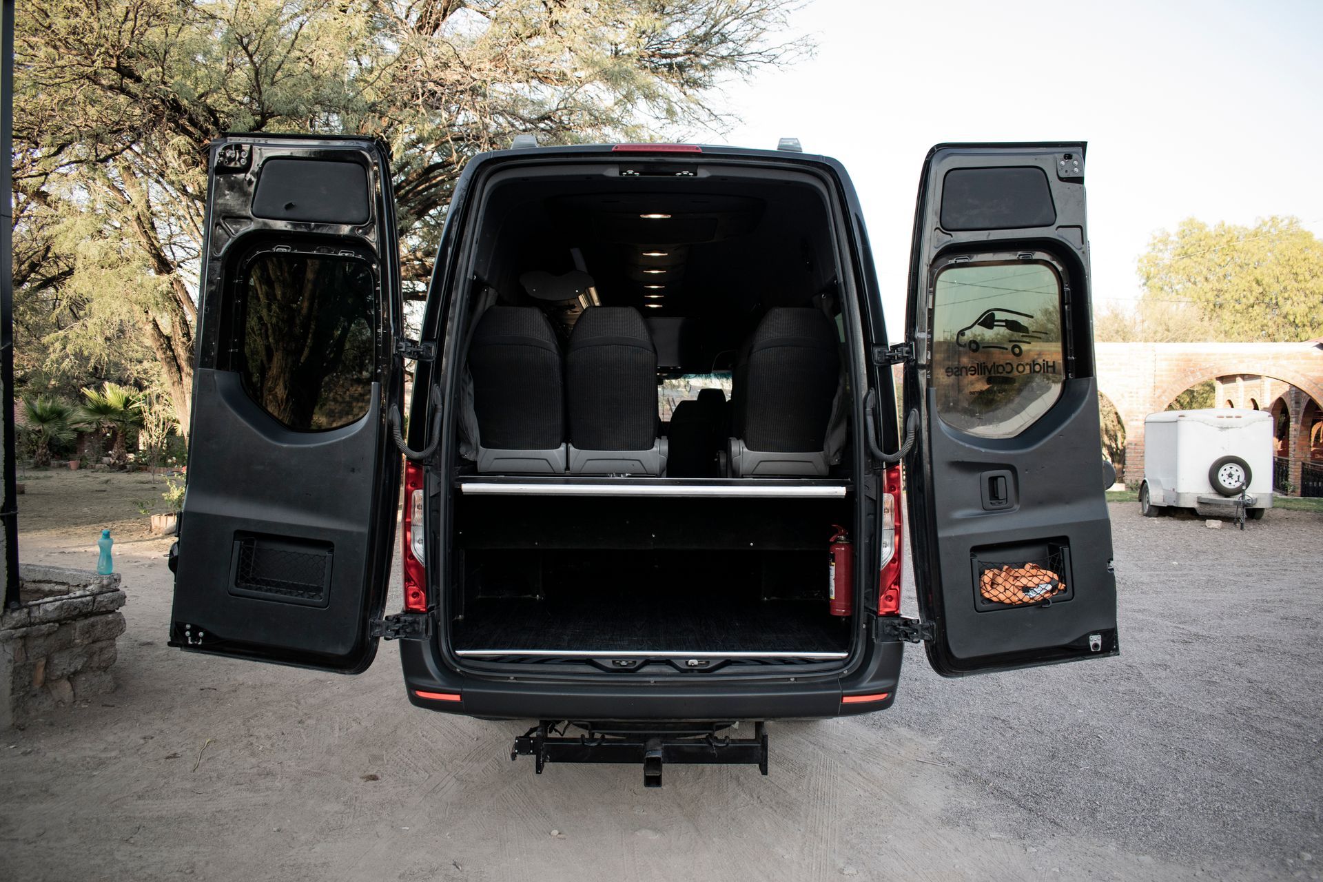 A black van with its doors open is parked in a gravel lot.