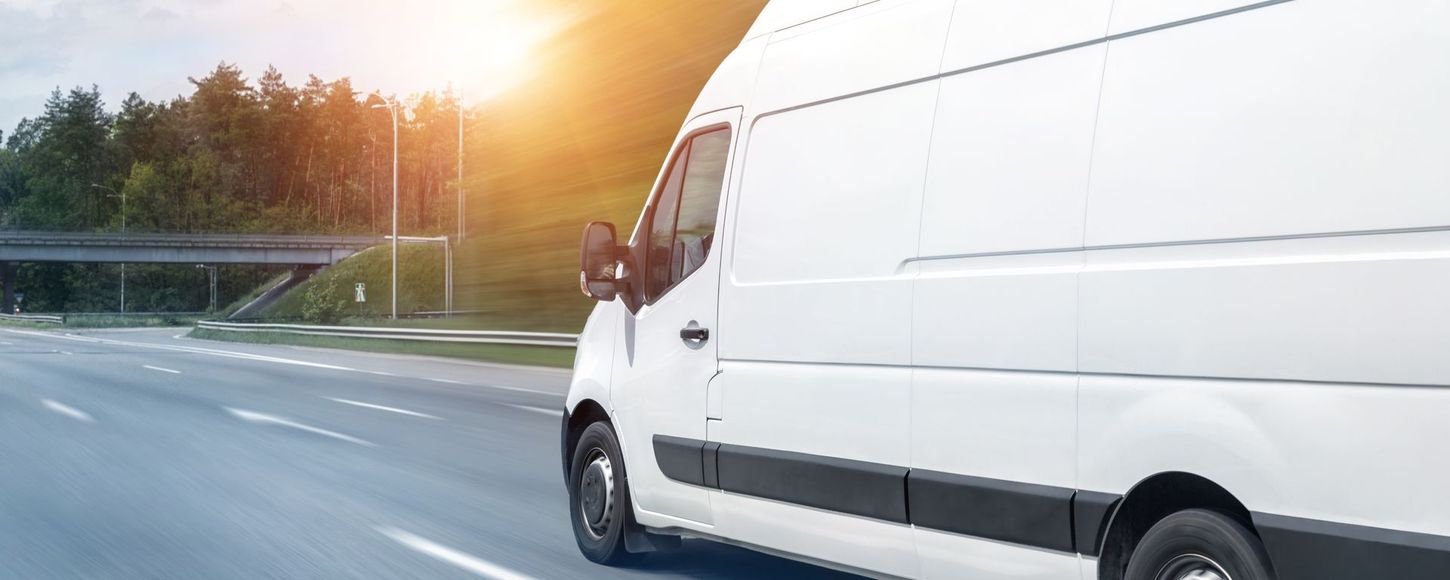 A white delivery van is driving down a highway.