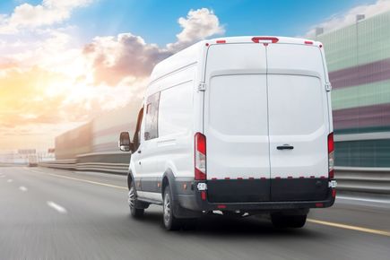 A white delivery van is driving down a highway.