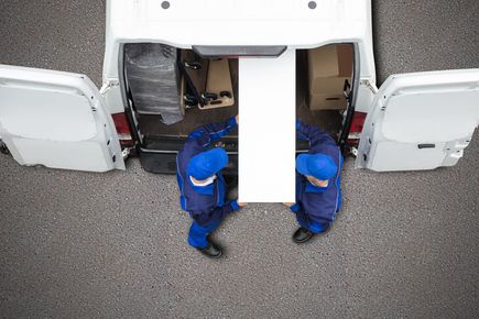 Two men are carrying a large piece of wood into a van.