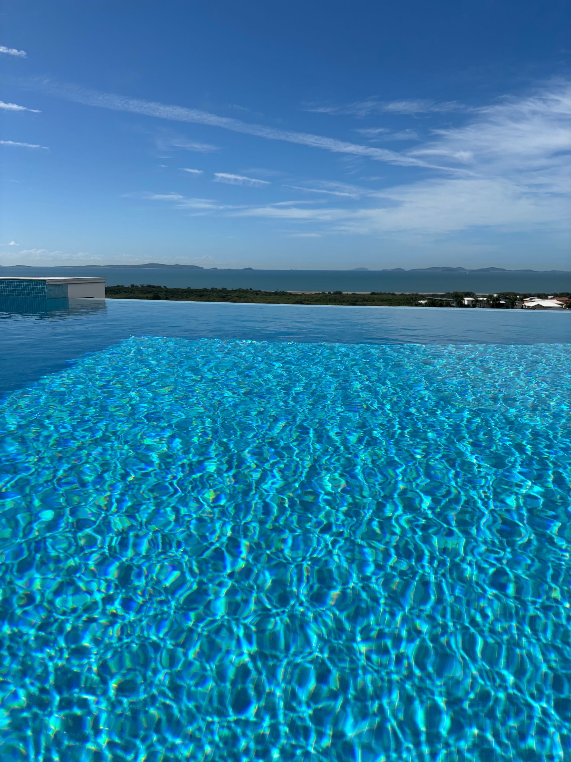 An infinity pool with vibrant blue water overlooking the ocean under a clear, bright blue sky. Pool Maintenance in Pacific Heights, QLD