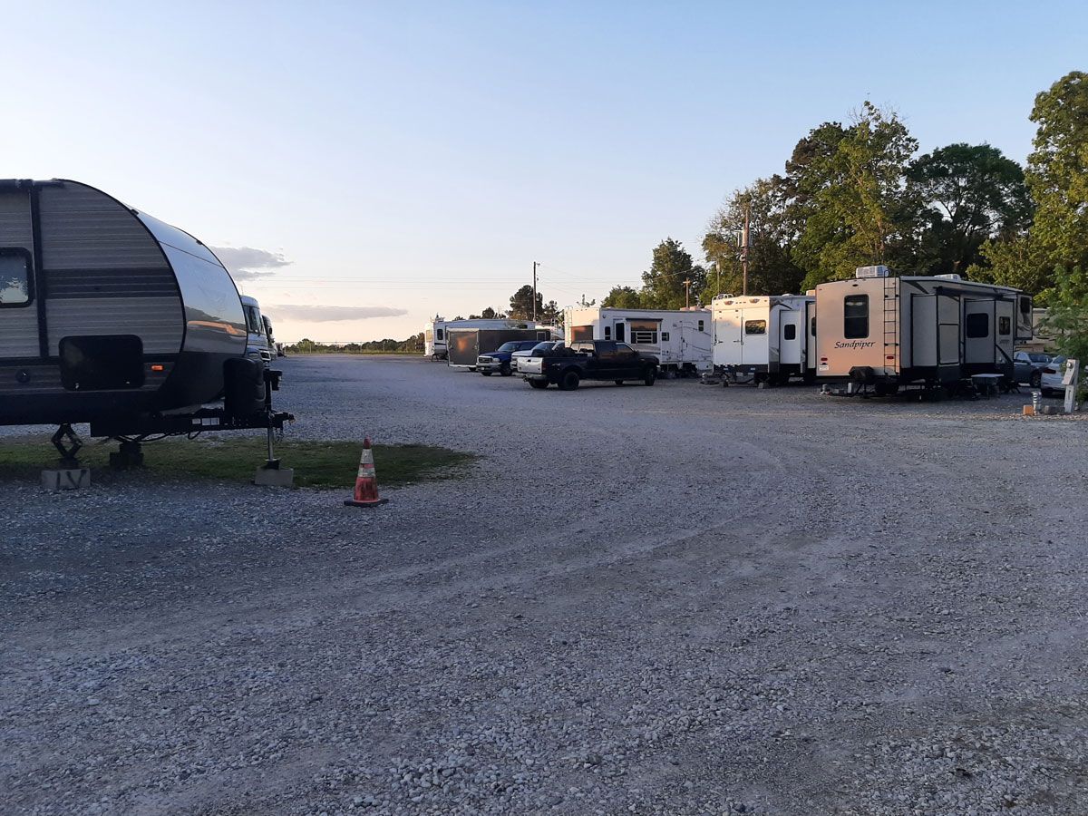 RV campground with several parked trailers on a gravel lot, trees in the background.