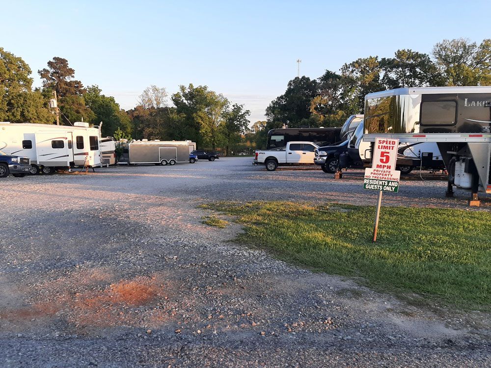 A gravel parking lot with RVs, trucks, and trees under a clear sky.