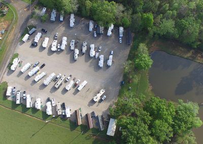 Aerial view of RV park with many white RVs parked near green trees and a body of water.