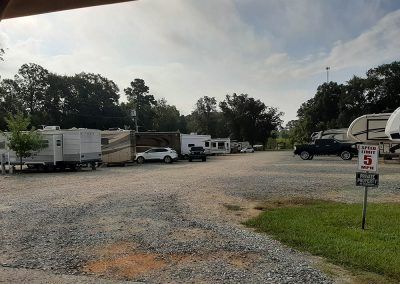 RV park with gravel parking. RVs are parked in rows. A white SUV and a black pickup truck are visible.