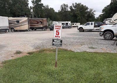 Speed limit sign 5 MPH in RV park with parked campers, trucks, and grassy foreground.