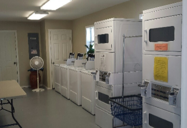 A laundromat with several white washing machines and dryers; a fan, table, and baskets are also visible.