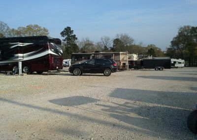 RV park with parked RVs, a black SUV, and gravel ground under a blue sky.