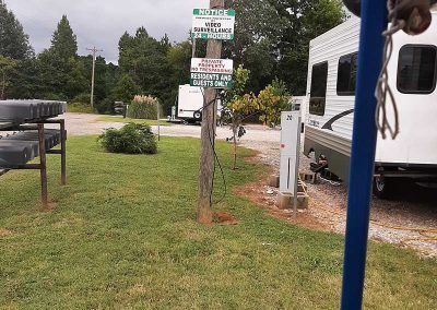 RV campsite with a sign post, RVs, grass, and trees.