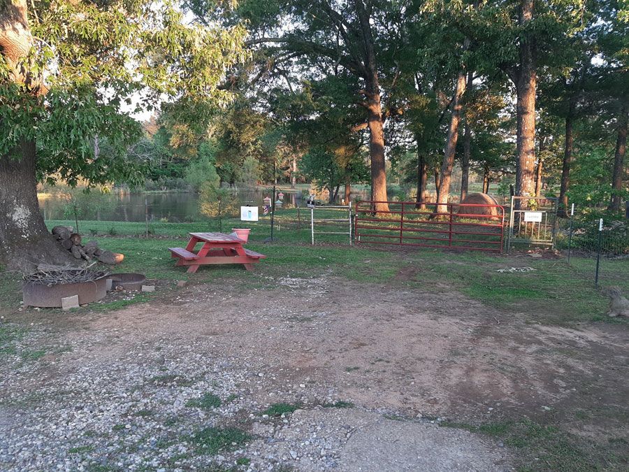 Picnic area with red table, bench, and fence in a wooded area.