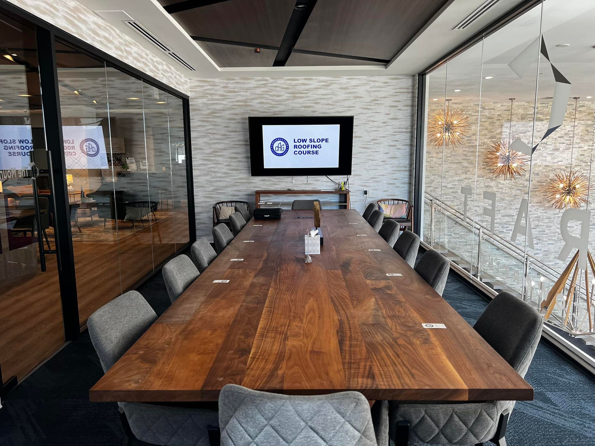 Conference room with long wooden table, chairs, TV, and glass walls.