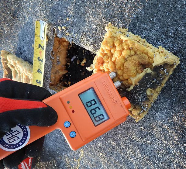 A hand holding a radiation detector near yellow, charred foam on asphalt; reading 86.8. A ruler is visible.