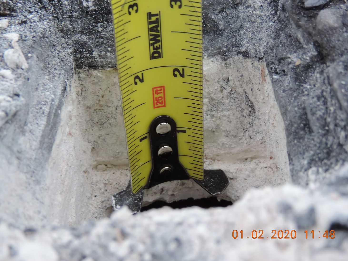Hand holding a moisture meter measuring 27.9 on a piece of wood. A tape measure is visible in the background.
