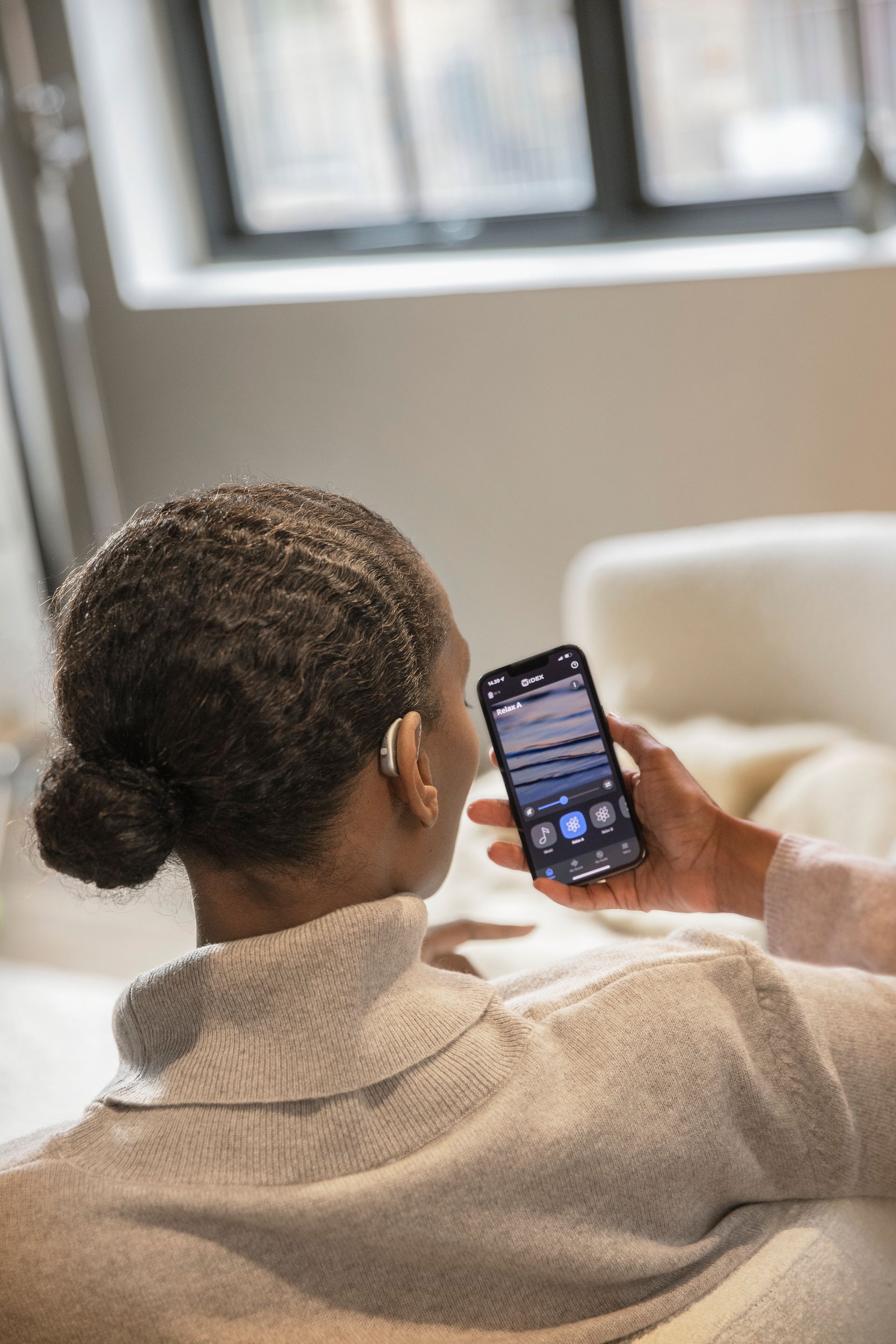 Una donna è seduta su un divano e tiene in mano un cellulare.