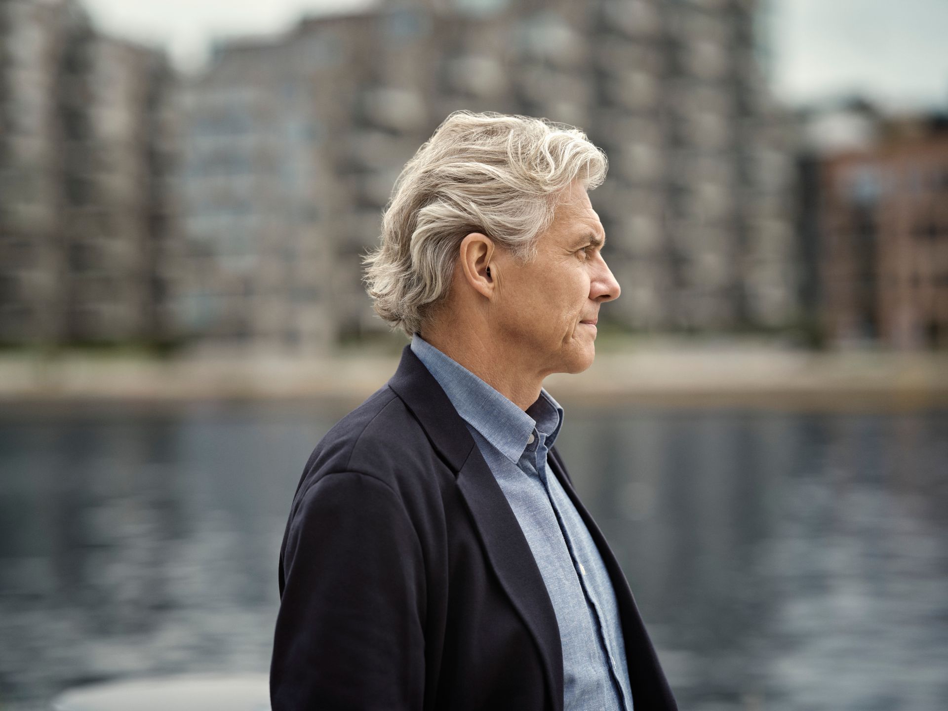 Un uomo in giacca e cravatta è in piedi davanti a uno specchio d'acqua.