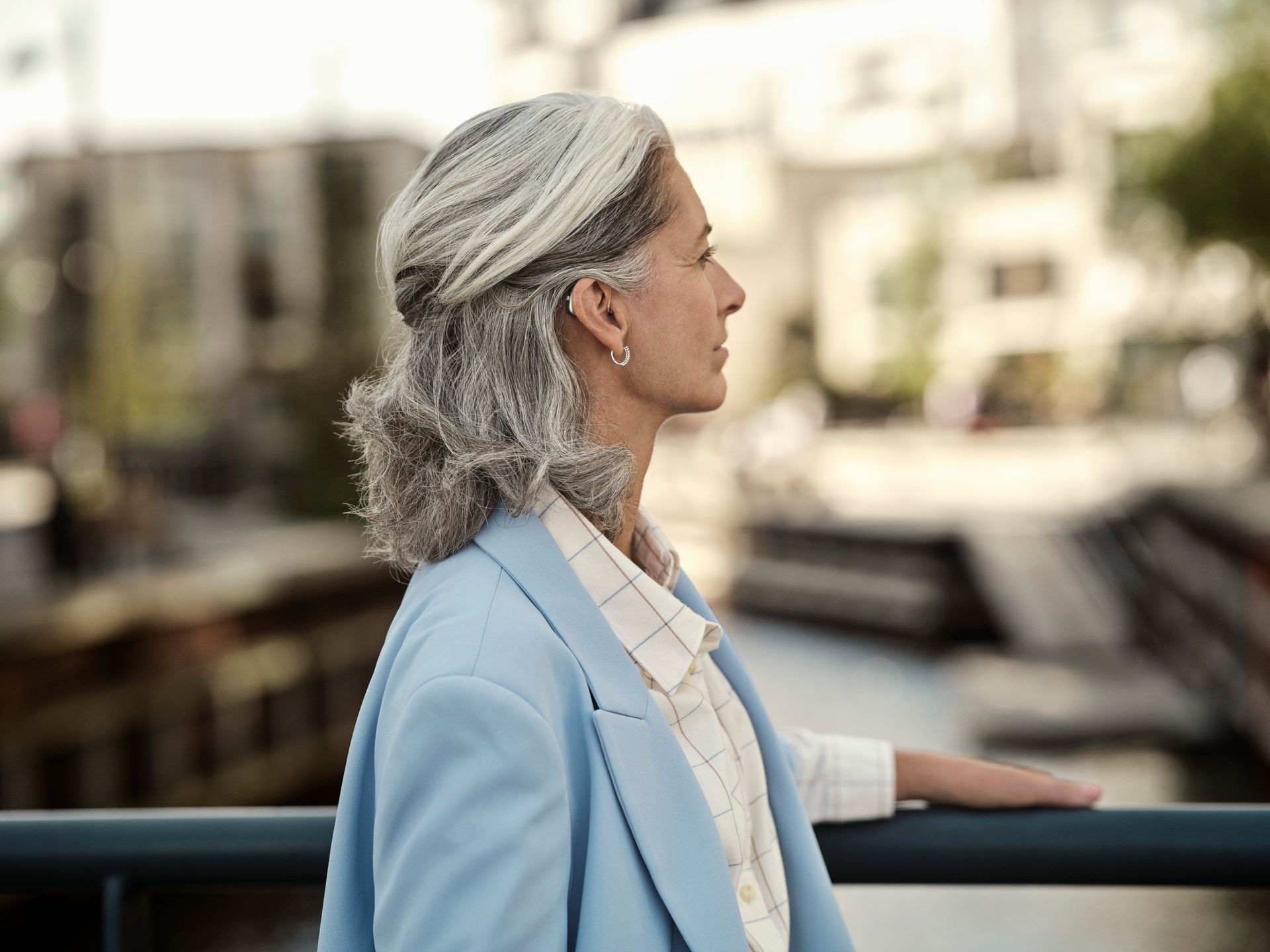 Una donna con i capelli grigi e una giacca blu è appoggiata a una ringhiera.