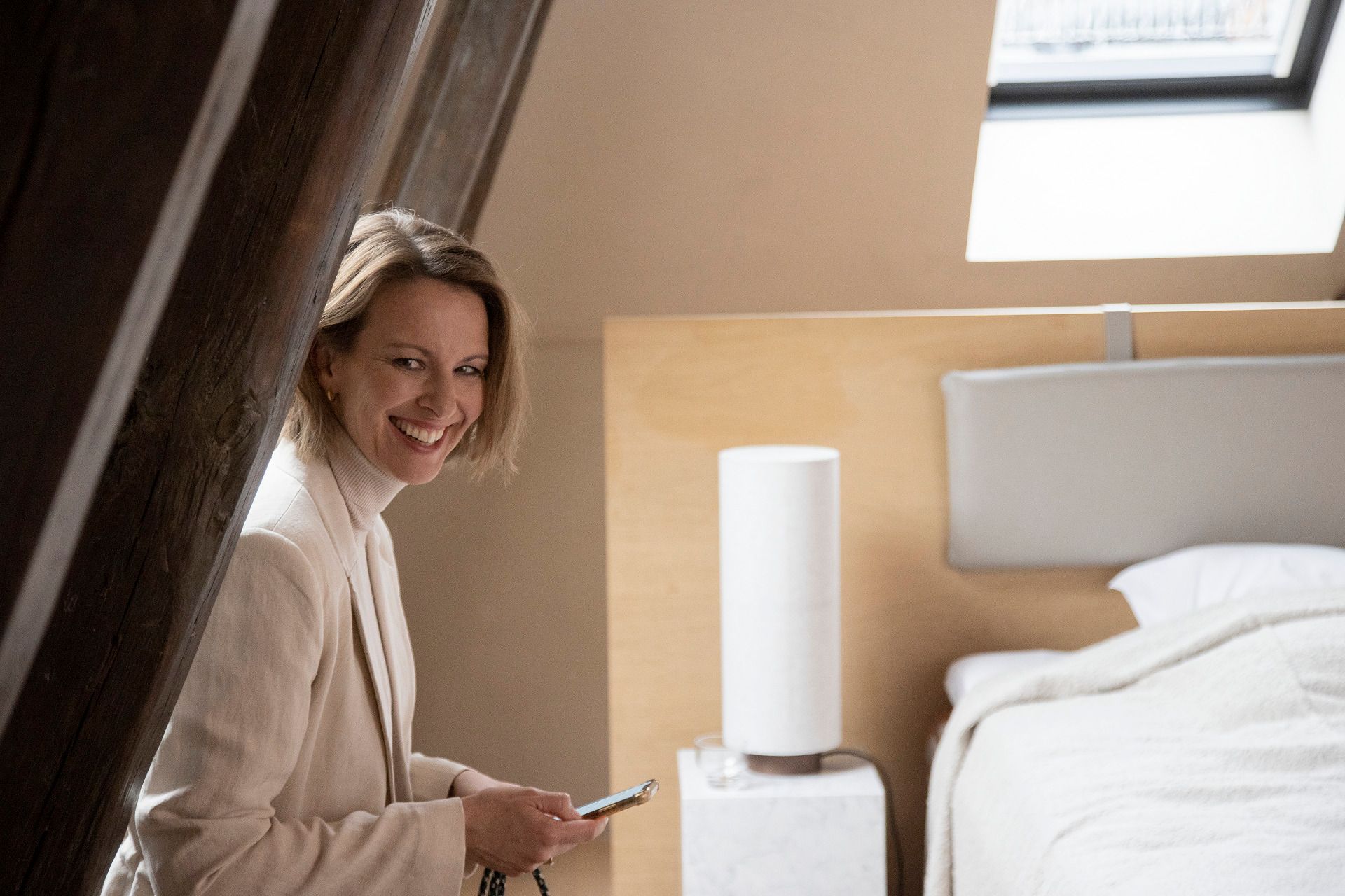 Una donna è seduta in camera da letto e guarda il suo telefono.