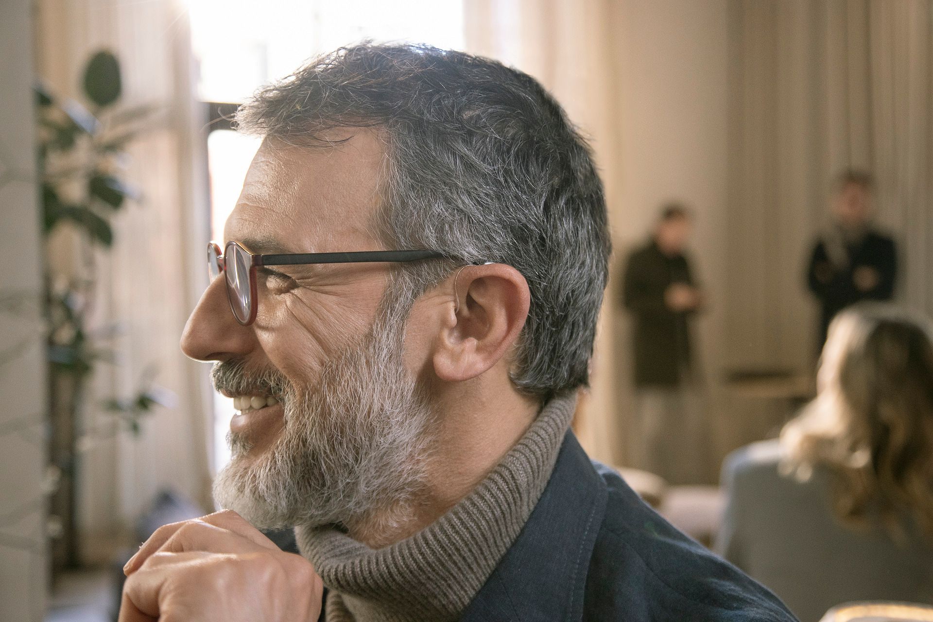 Un uomo con la barba e gli occhiali sorride in un soggiorno.