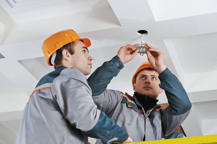 two men are working on a light fixture on the ceiling