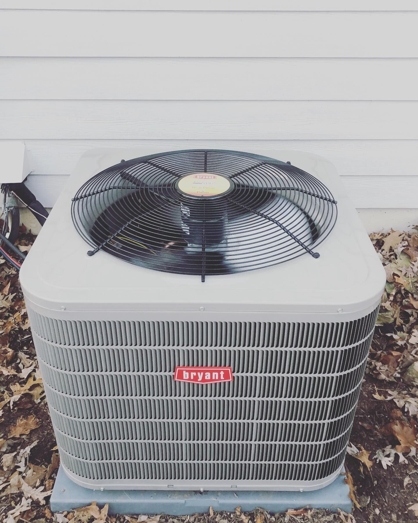 A bryant air conditioner is sitting outside of a house.