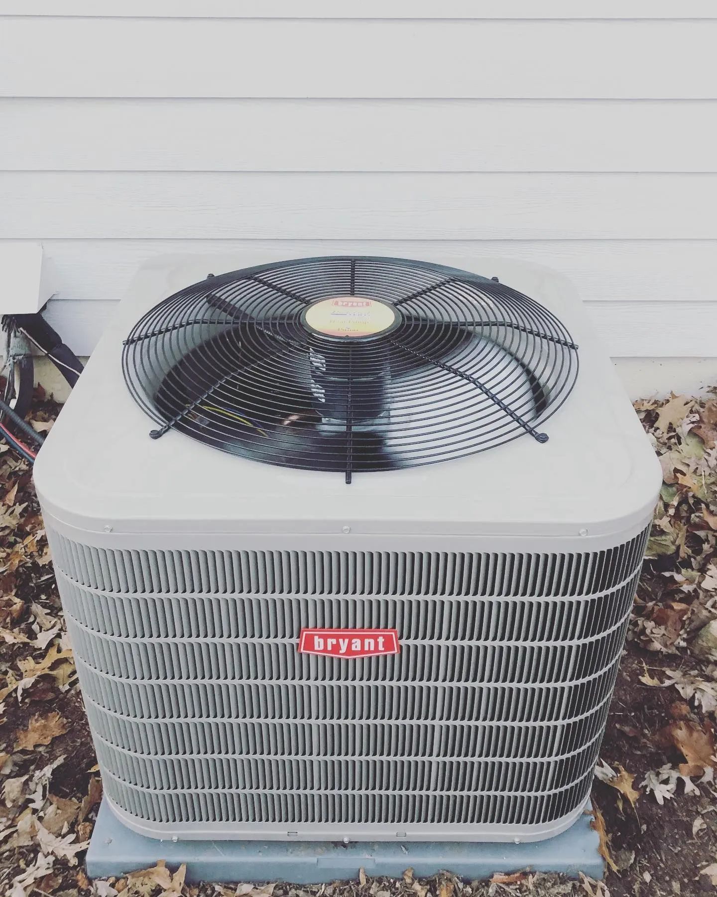 Bryant air conditioning unit outside a white house, with black fan and red logo.