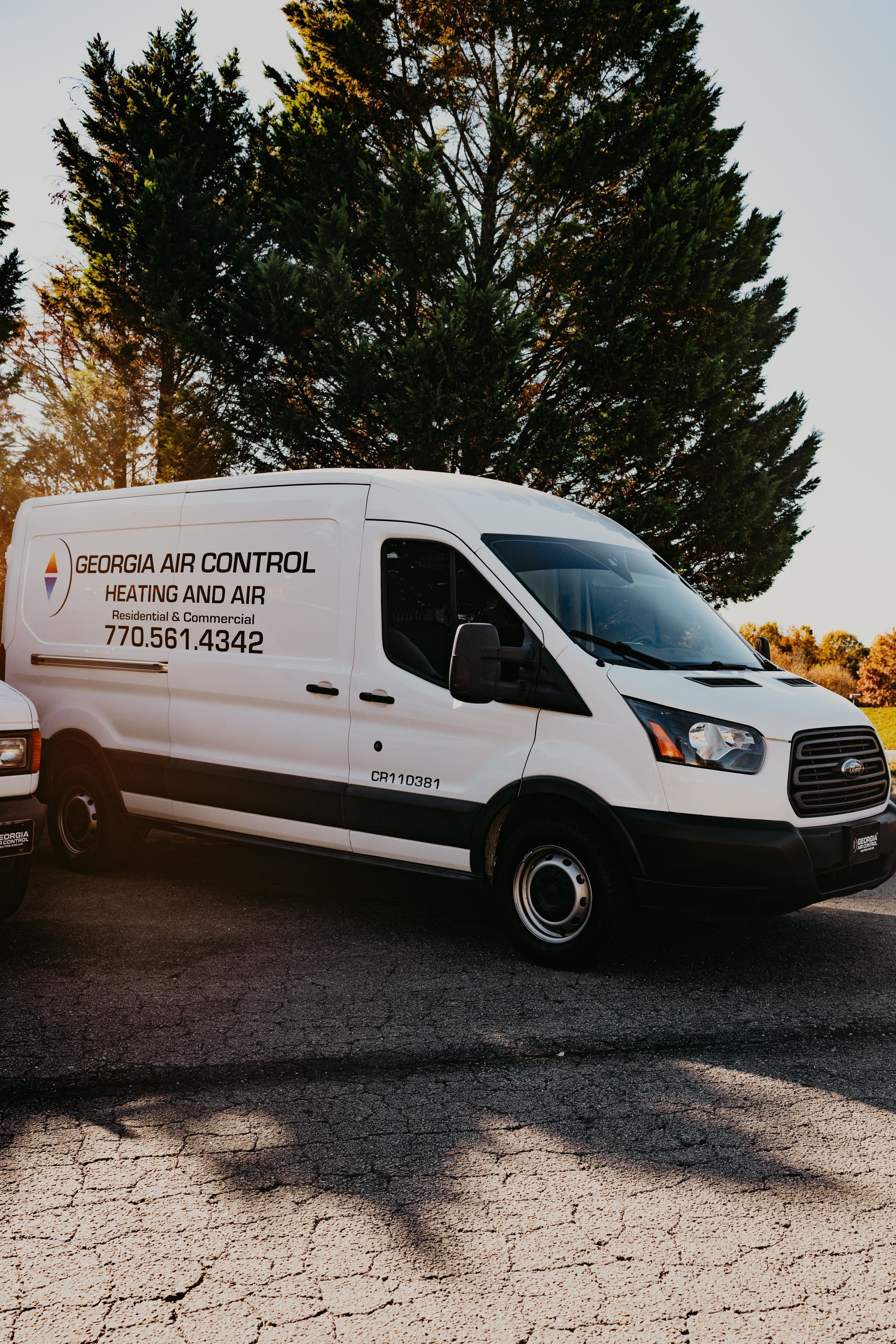 A white van is parked in a gravel lot next to a tree.