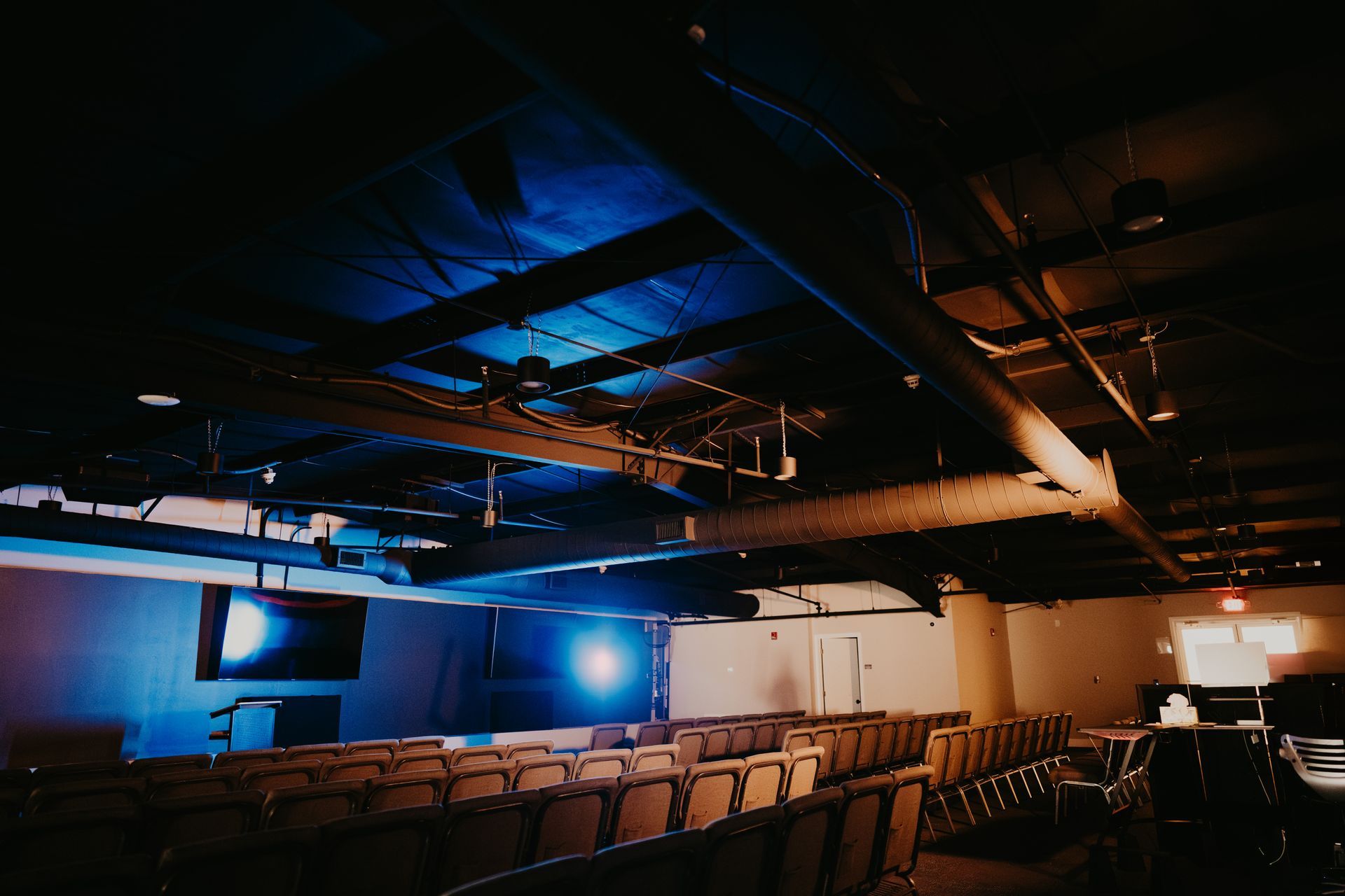 An empty auditorium with rows of seats and a blue light coming from the ceiling.