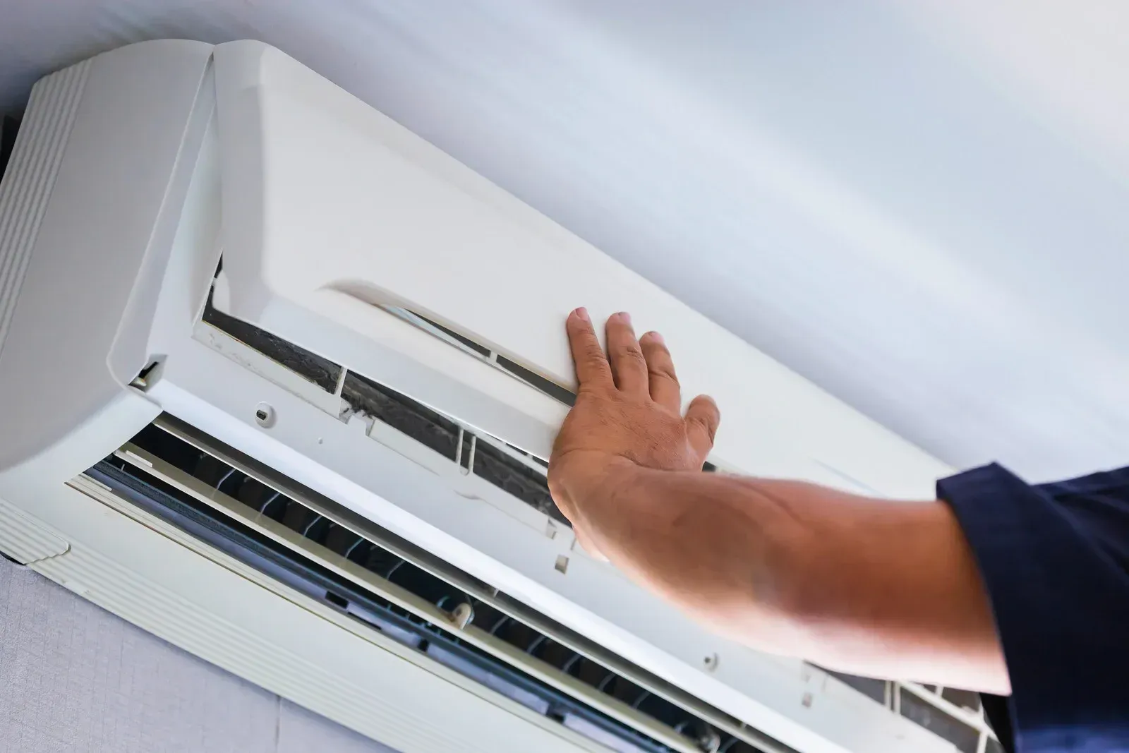 A person's hand touching a white, wall-mounted air conditioning unit.
