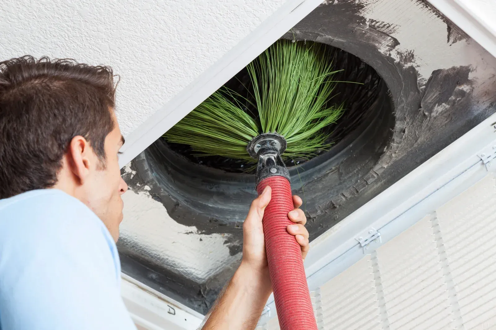 A man is cleaning an air vent with a brush.