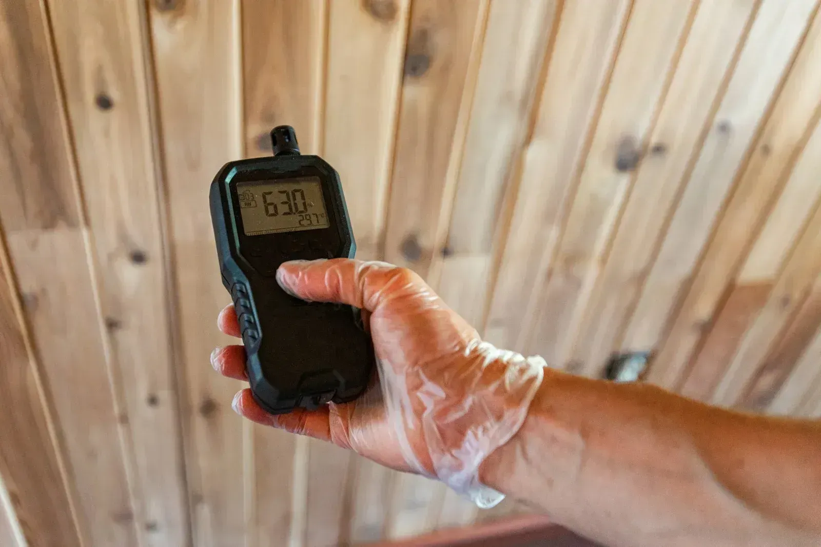 A person is holding a remote control in their hand in front of a wooden wall.