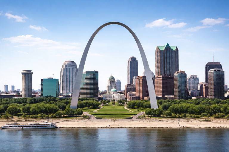 The Gateway Arch in St. Louis, Missouri, over a cityscape with a river in the foreground, under a blue sky.