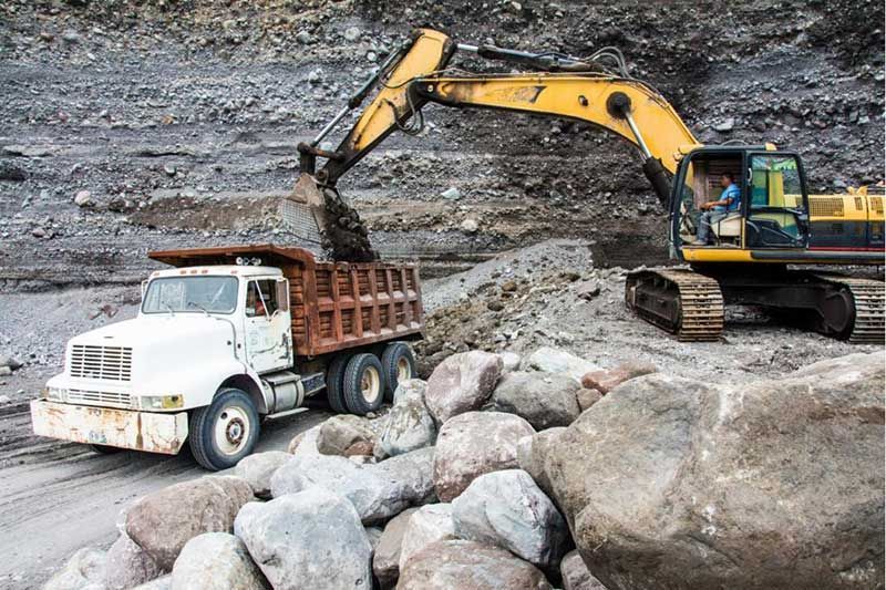 Una excavadora carga un camión volquete con piedras.