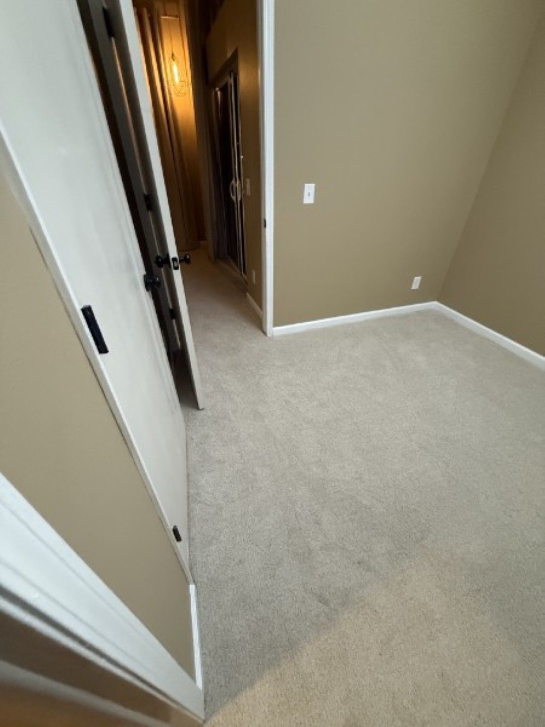 Beige carpeted hallway with white doors and tan walls, viewed from an open doorway.