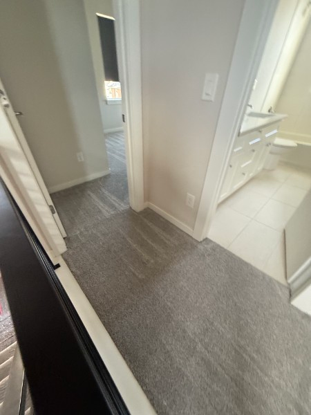 Narrow hallway with gray carpet leading to a doorway beside a white bathroom vanity and tiled floor.